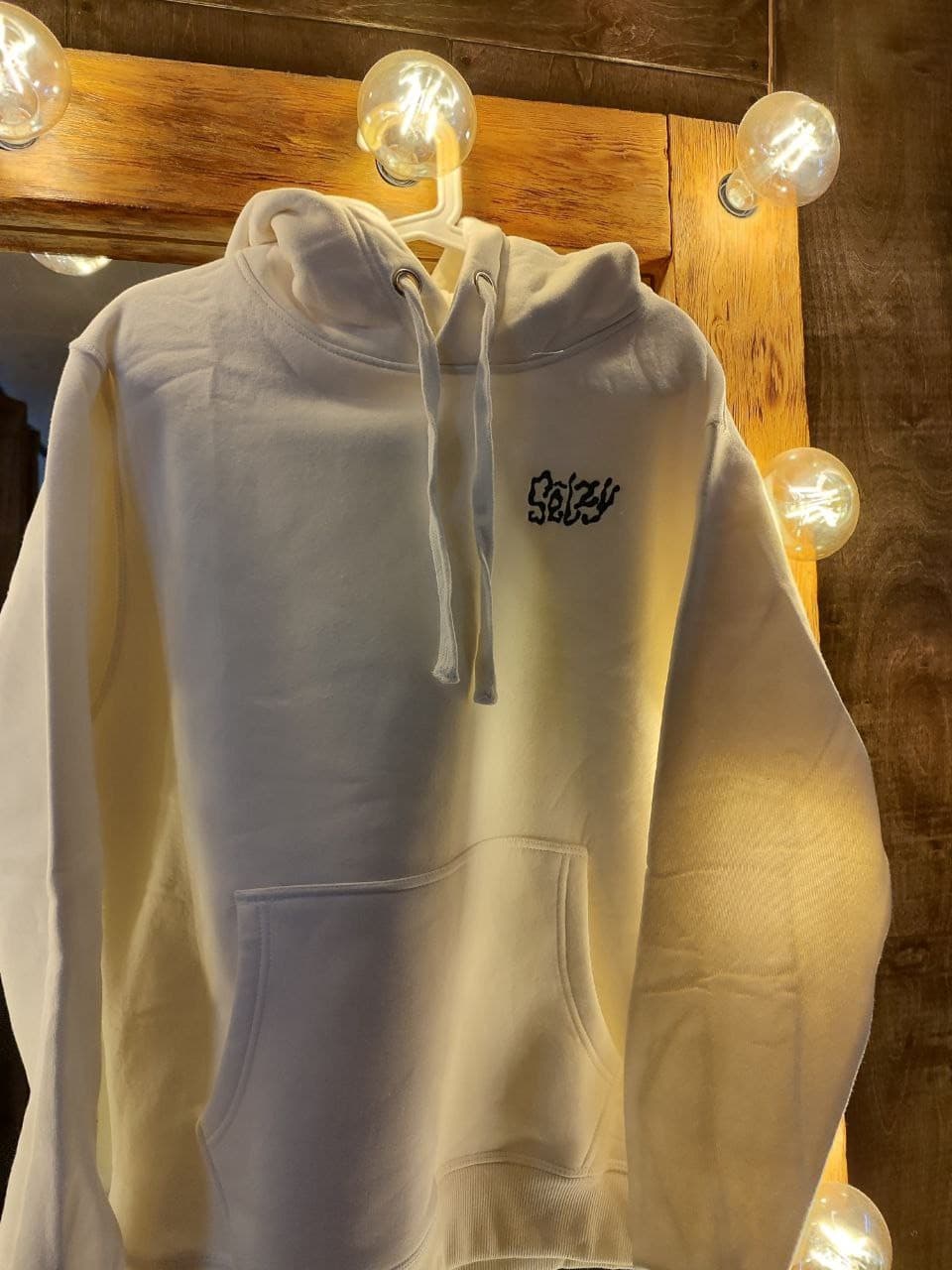 Cream Selzy hoodie from the front, by a mirror with bulb lights